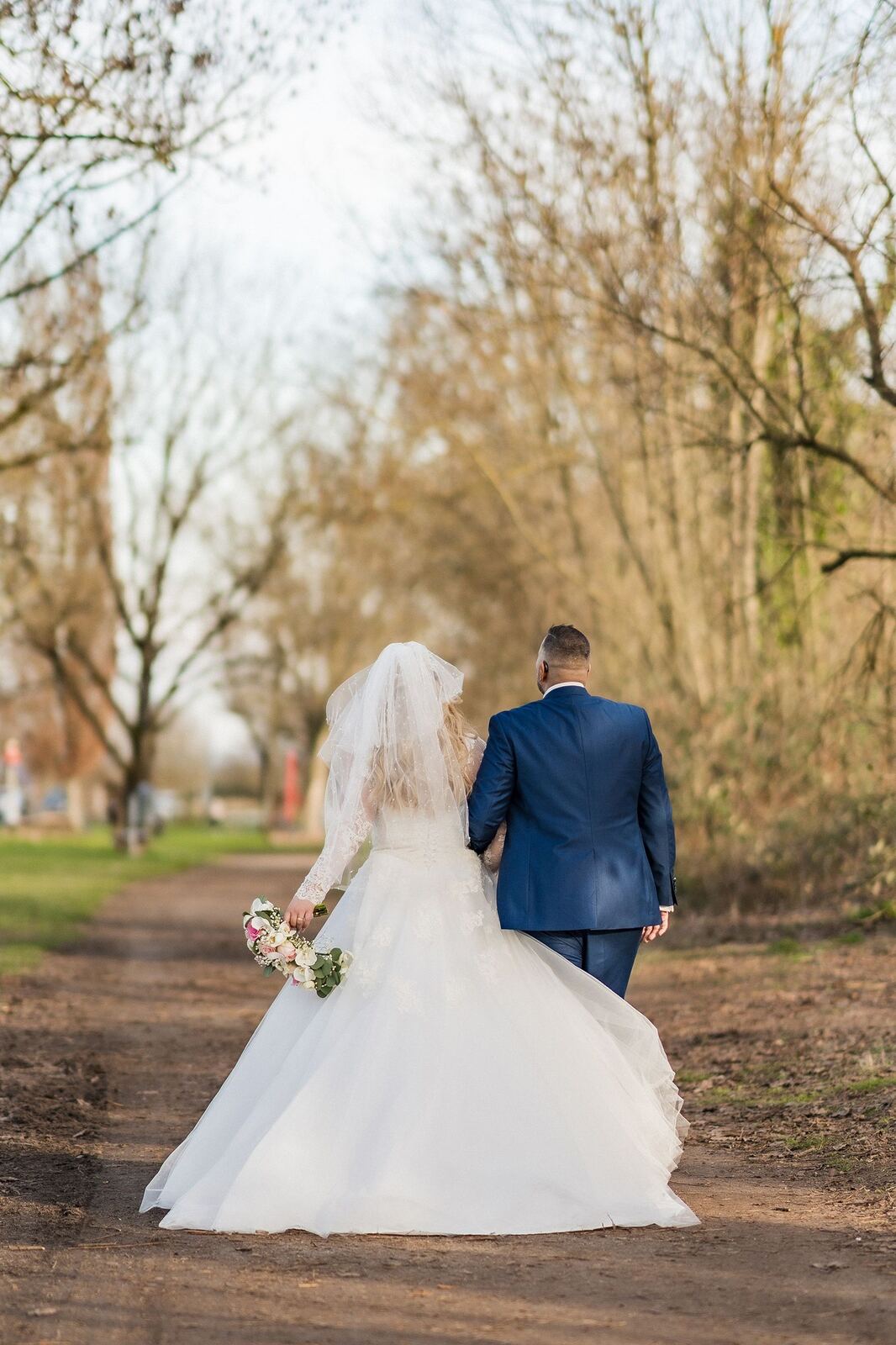 Bride and groom walking together down a tree-lined path
